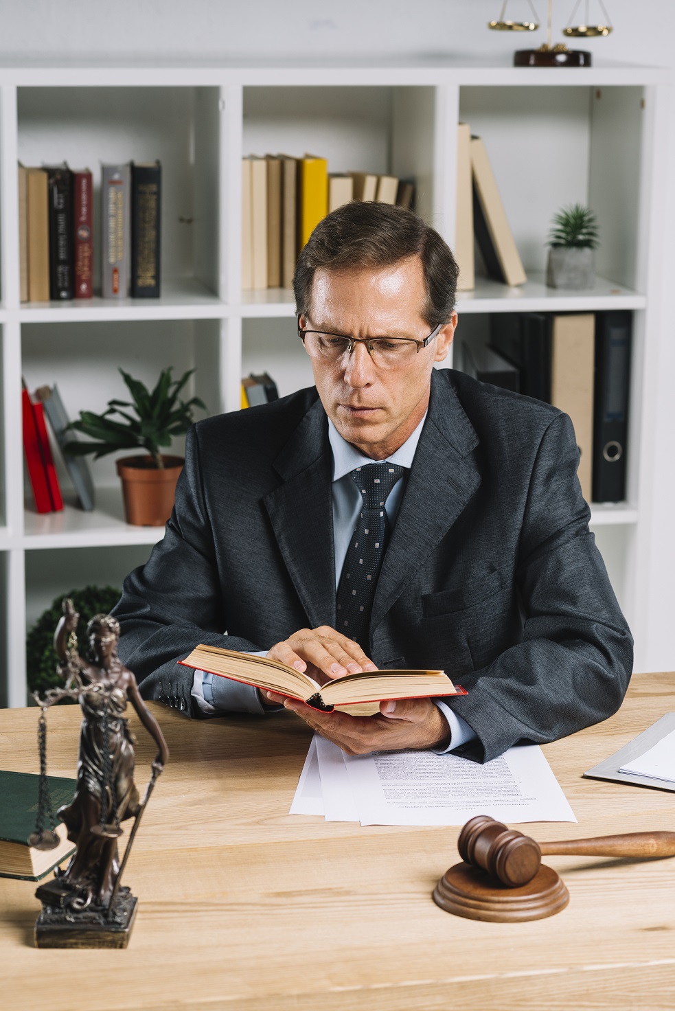 mature-male-lawyer-reading-book-with-gavel-and-justice-statue-on-wooden-table